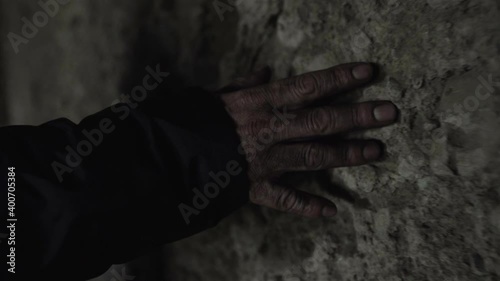 Man touching his hand across a stone wall in a dark, moody cave. Mysterious, eerie, atmoshperic scene.