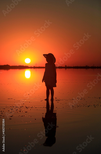 Silhouette of a little girl in the water of the lake at sunset