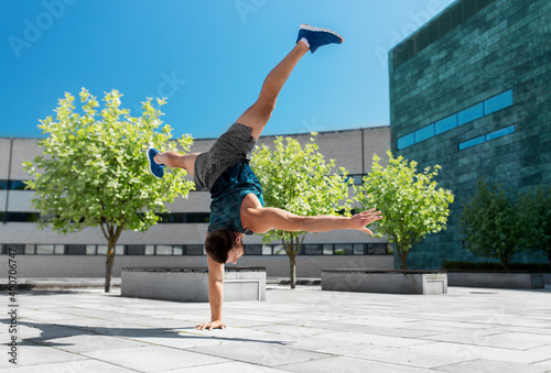 fitness, sport, training and lifestyle concept - young man exercising and doing handstand on one arm outdoors