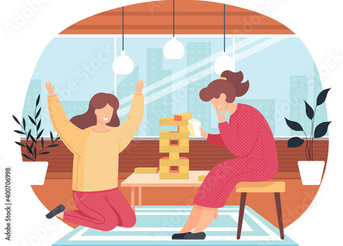 Girls are playing Jenga at home. The woman in yellow win and raises her hands up. Two funny girlfriends spend time together. Fantastic turn-based board game. Friends having fun at the weekend