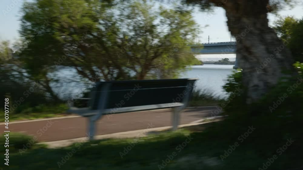 Approach major traffic bridge as you journey along tree lined bank of beautiful Canning River with walkers along foreground path. Jetty visible Approach major traffic bridge as you journey along tree lined bank of beautiful Canning River with walkers along foreground path. Jetty visible