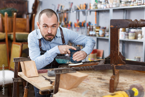 Professional furniture restorer in process of renovation vintage armchair in workshop