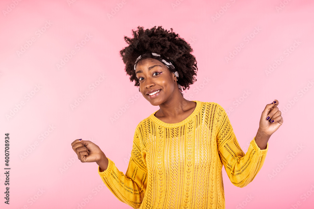 Confident happy young black woman posing in yellow winter sweater over pink studio background