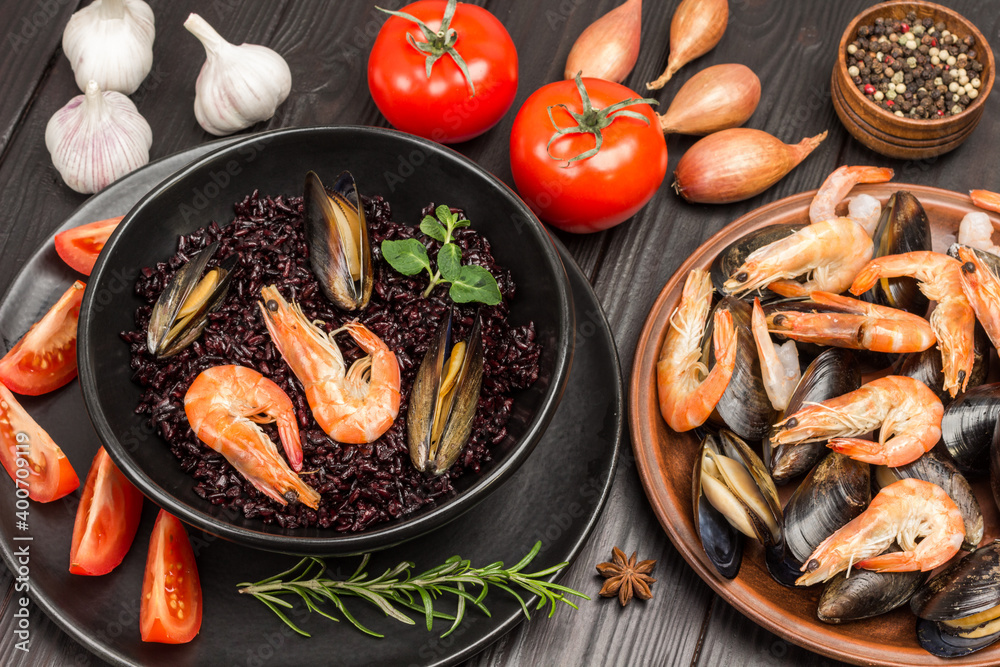 Shrimp and mussels with black rice in bowl. Tomatoes, onions and garlic on table. Mussels and shrimps in plate Shrimp and mussels with black rice in bowl. Tomatoes, onions and garlic on table. Mussels and shrimps in plate