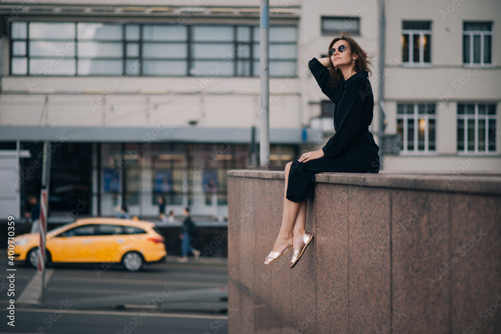 Young woman in black dress sitting, have a break in city Young woman in black dress sitting, have a break in city