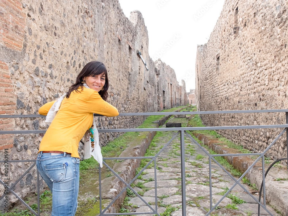 Fototapeta premium Rear view of a woman in yellow clothes leaning on metallic fence while exploring ancient ruins