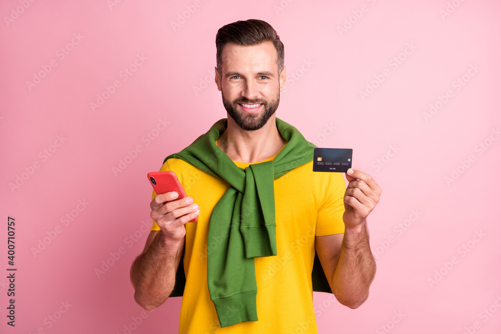 Photo of handsome brown haired bearded man wear jumper on shoulders hold credit card phone isolated on pink color background Photo of handsome brown haired bearded man wear jumper on shoulders hold credit card phone isolated on pink color background