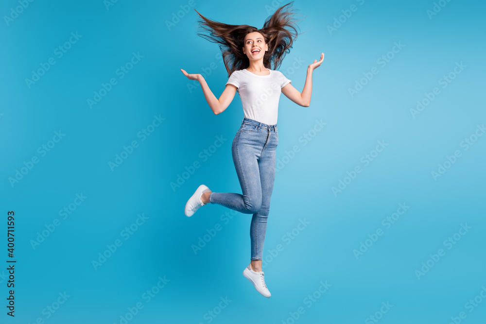 Full size photo of charming woman fly hair jump up look empty space isolated on blue color background Full size photo of charming woman fly hair jump up look empty space isolated on blue color background