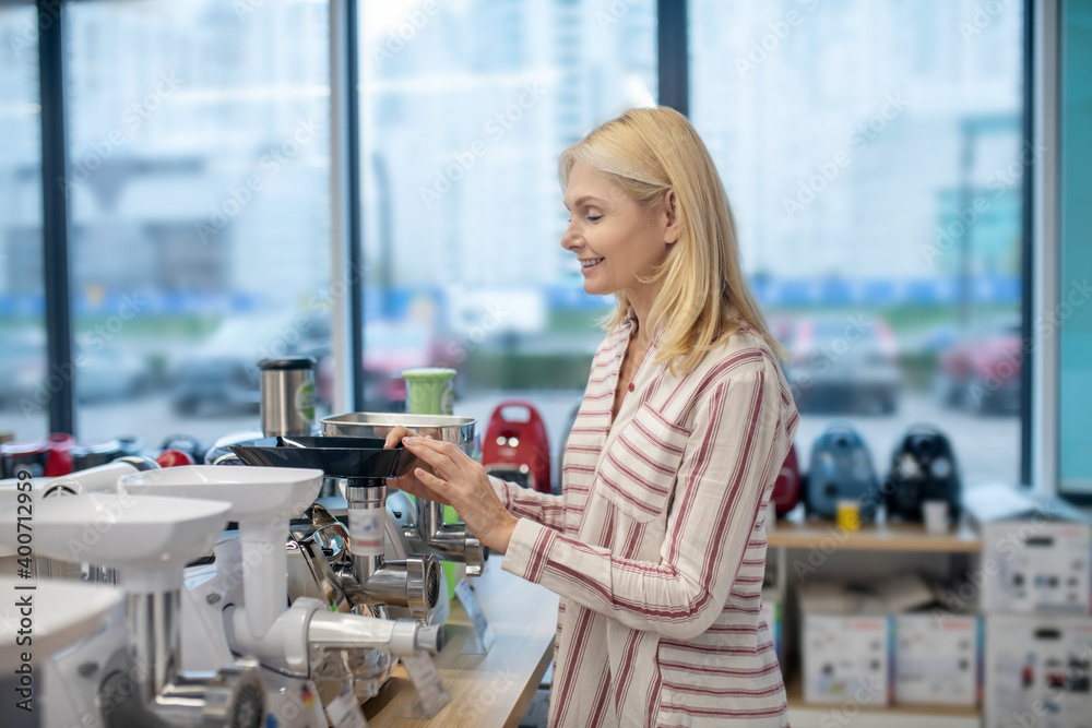 Blonde female customer standing in a consumer goods showroom and choosing a mincing machine
