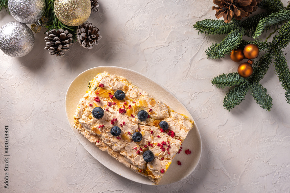 Homemade Meringue roll cake with cream, berries and almond on plate, selective focus, in the background Christmas tree branches with cones and toys, top view Homemade Meringue roll cake with cream, berries and almond on plate, selective focus, in the background Christmas tree branches with cones and toys, top view