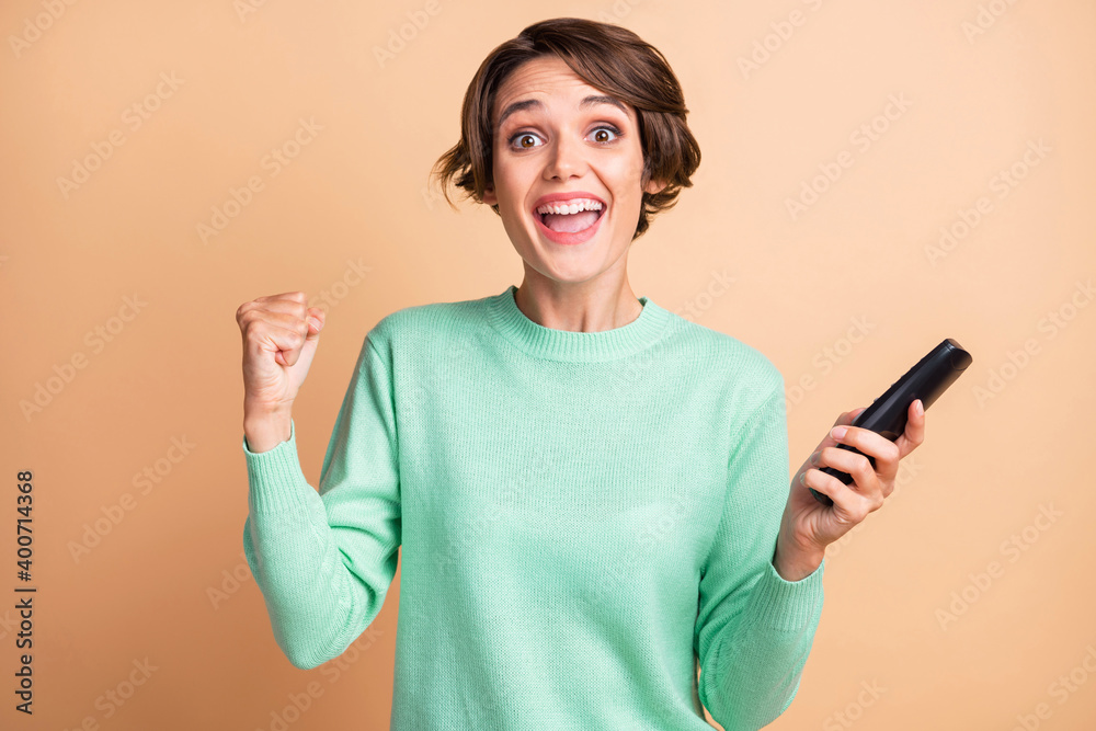 Photo of young girl excited happy win goal fists hand hold remote control wear teal pullover isolated over beige color background Photo of young girl excited happy win goal fists hand hold remote control wear teal pullover isolated over beige color background