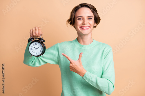 Photo of young girl happy smile indicate point index finger clock advert promo decision recommend isolated over beige color background photo