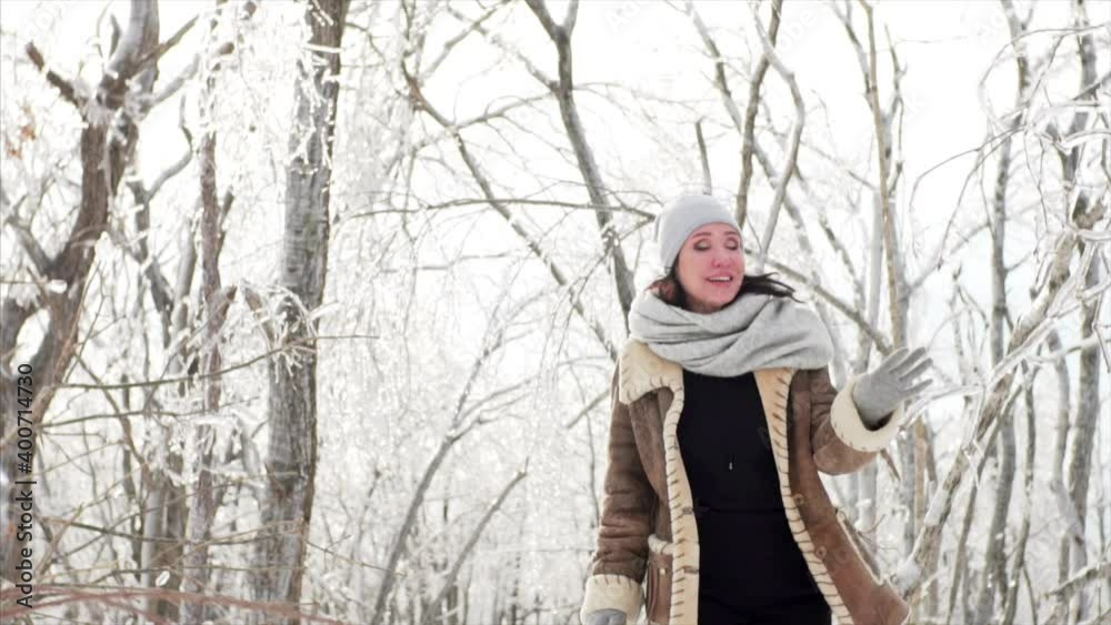 Happy middle-aged woman is looking into the camera and dancing in the forest where branches are covered with ice after icy rain, natural disaster. Russia Happy middle-aged woman is looking into the camera and dancing in the forest where branches are covered with ice after icy rain, natural disaster. Russia