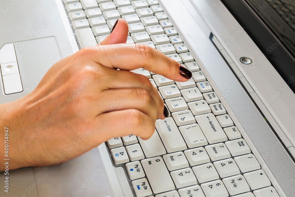 A woman's hand is typing on a laptop keyboard. Analyze information before pressing the A woman's hand is typing on a laptop keyboard. Analyze information before pressing the