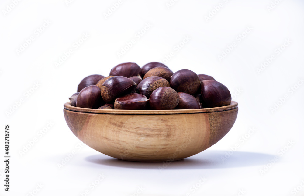 Obraz premium Chestnuts in a wooden bowl on white background. Castanea sativa, sweet ripe Chestnuts