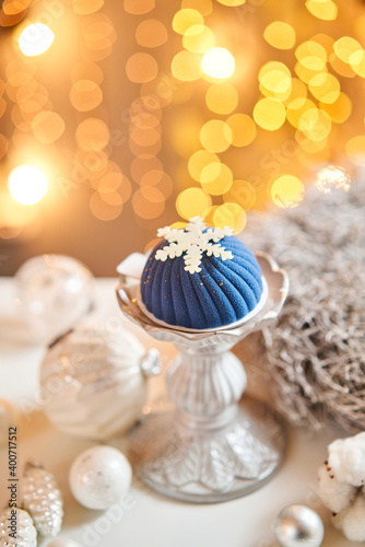 Mini mousse pastry dessert covered with blue velour on garland lamps bokeh background. Modern european cake. French cuisine. Christmas theme