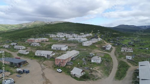 A view of the abandoned village located between the hills. There are two-storey houses and one-storey wooden houses in the village. Many houses have been destroyed. There is a lot of metal debris arou photo