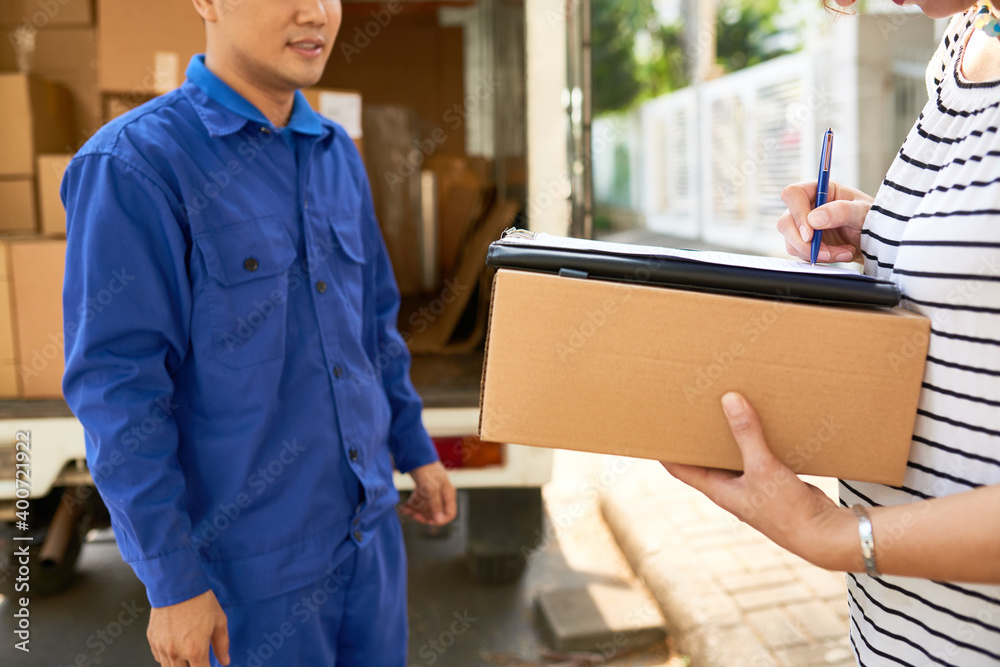 Moving house company courier in blue uniform looking at woman signing delivery service documents Moving house company courier in blue uniform looking at woman signing delivery service documents