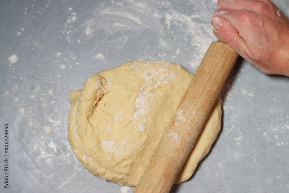 woman rolls out dough with rolling pin on table, close-up woman rolls out dough with rolling pin on table, close-up