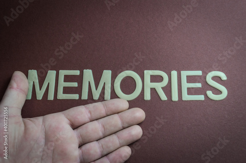 Human hand showing the word Memories written with plastic letters on brown paper background