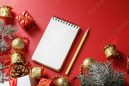 Notepad and pencil for writing wishes and gifts for the New Year and Christmas around the Christmas tree decorations on a red background.