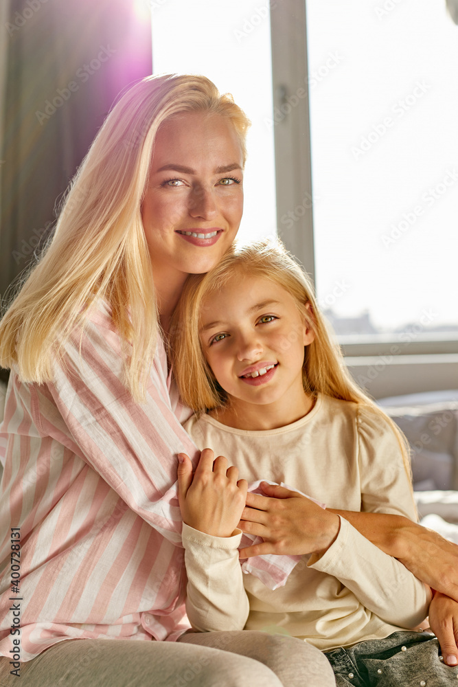 optimistic happy mother with child girl on bed, caucasian blond female hugs her cute daughter, they are smiling optimistic happy mother with child girl on bed, caucasian blond female hugs her cute daughter, they are smiling