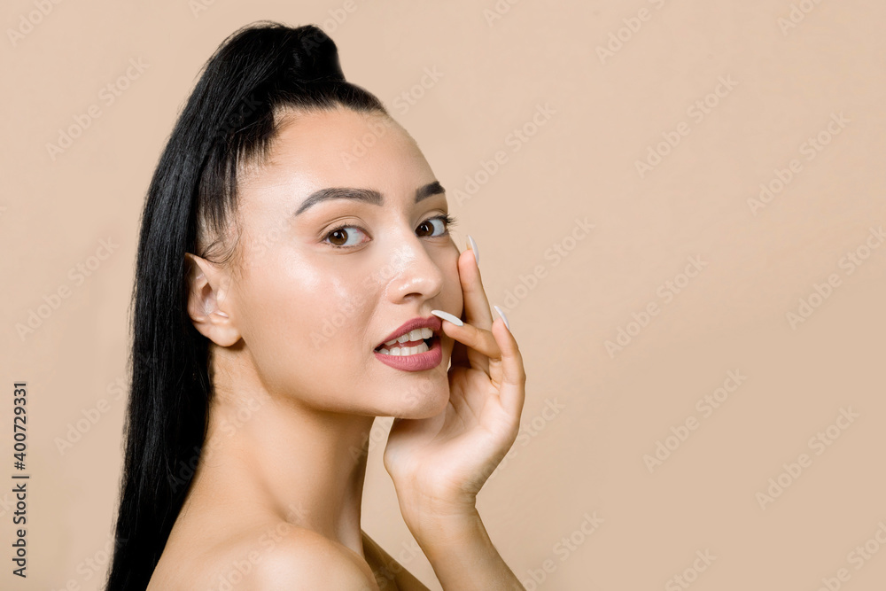Beautiful young asian girl with clean fresh skin and natural nude makeup, looks at camera with sexy smile, touching her lips, posing on beige background. Facial treatment, beauty and spa. Copy space Beautiful young asian girl with clean fresh skin and natural nude makeup, looks at camera with sexy smile, touching her lips, posing on beige background. Facial treatment, beauty and spa. Copy space