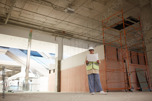 Wide angle portrait of contemporary female engineer looking at documents while standing on construction site, copy space