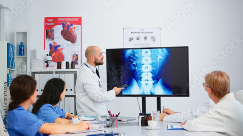 Cvalified head doctor in white coat sitting in hospital boardroom explaining spin functions pointing on digital x-ray image. discussing symptoms of disease for further treatment