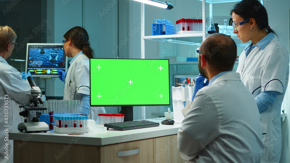 Obraz premium Team of microbiologists researching using computer with green screen overtime sitting in modern equipped lab. Doctors doing vaccine research writing on device with chroma key, isolated, mockup display