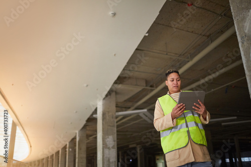 Graphic wide angle portrait of mixed-race female engineer using digital tablet while standing on construction site, copy space © Seventyfour