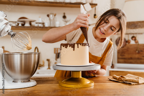 Canvas-taulu Beautiful pleased pastry chef woman making cake with chocolate cream