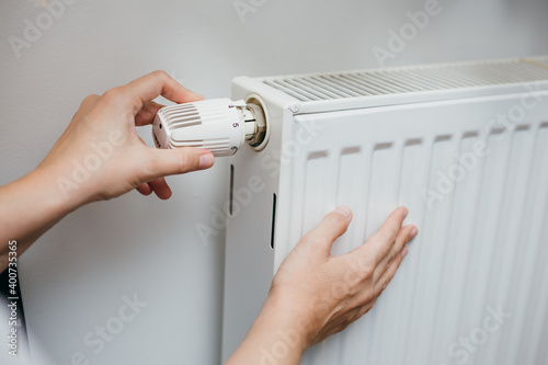 Close up shot of Caucasian female's hand adjusting radiator temperature using thermostat. Home with central heating.