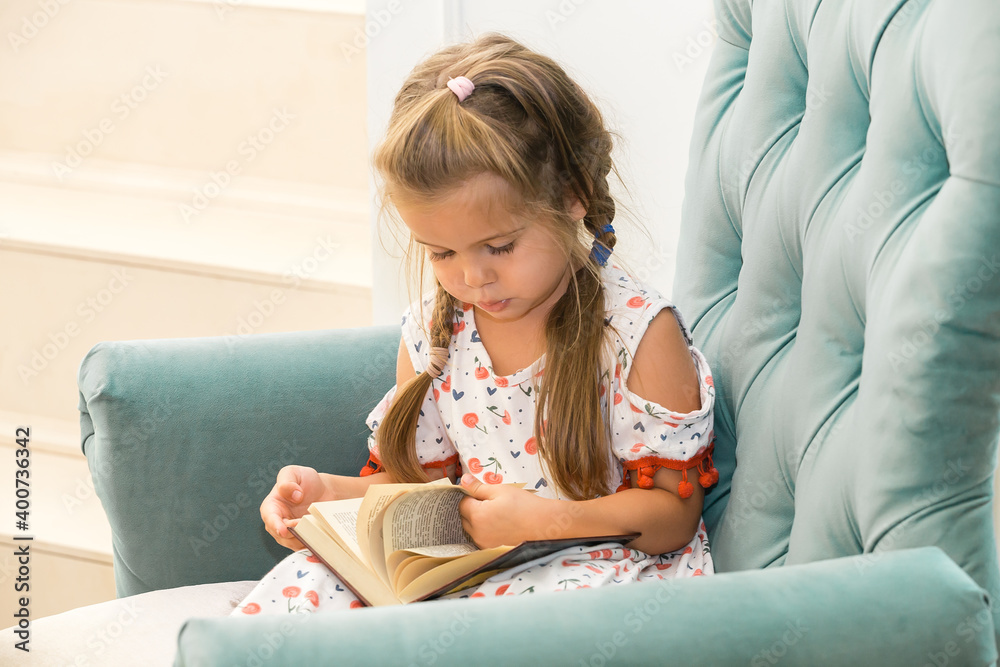 Little girl sitting in a green armchair and reading a large heavy book Little girl sitting in a green armchair and reading a large heavy book