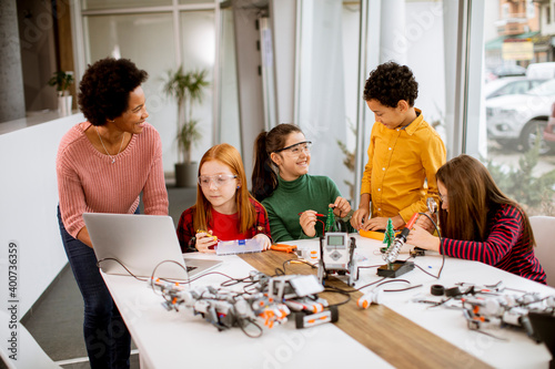 Happy kids with their African American female science teacher with laptop programming electric toys and robots at robotics classroom