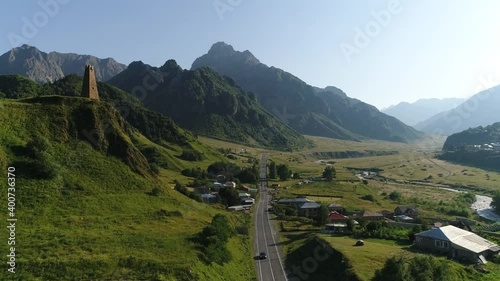 Small village situated among mountains, cars moving on a road. Aerial view