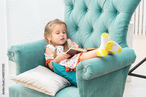 Foto A little girl lies in a green chair and reads a large heavy book