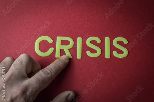 Human fingers pointing the word Crisis written with plastic letters on red paper background, concept