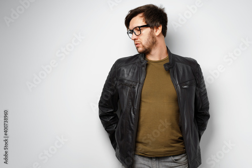 Portrait of a young man in glasses wearing black leather jacket on grey background