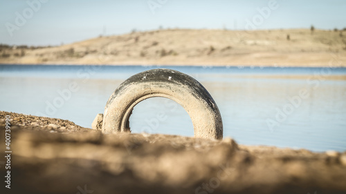 Old dirty car tire on the shore of a reservoir.