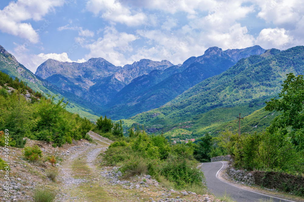 Summer landscape - valley and road in Albanian mountains, green trees and gray clouds on the sky