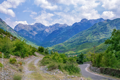 Summer landscape - valley and road in Albanian mountains, green trees and gray clouds on the sky
