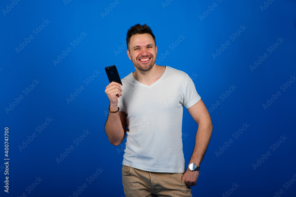 Handsome young man in a smart casual wear holding smart phone and looking at camera with smile Handsome young man in a smart casual wear holding smart phone and looking at camera with smile