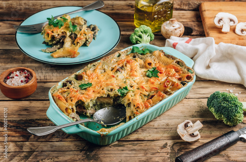 Homemade vegetarian casserole with pasta, mushrooms, broccoli sauce and cheese on a rustic wooden background. Selective focus