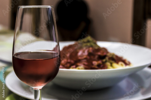 Glass of rose wine and a plate of pasta with tomato, meat and spices.