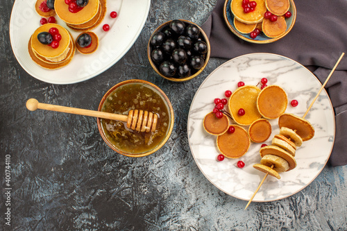 Family breakfast with fruit pancakes honey in a bowl and black cherries on gray table above view photo