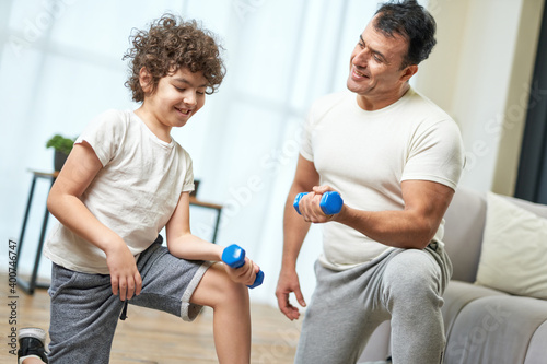 Family workout. Sportive latin middle aged father teaching his son exercising with dumbbells while spending time together at home