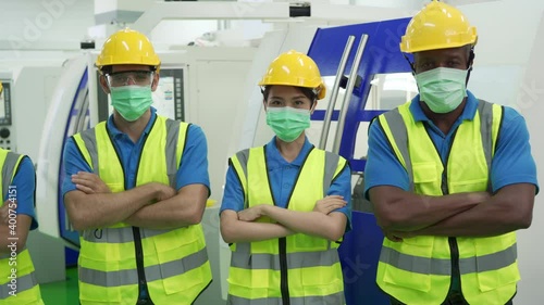 Diverse group of production line worker in factory wear helmet and face mask working at machine. New normal working concept in industry after Covid-19 Coronavirus pandemic outbreak