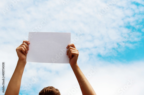 a blank sheet of paper in the hands of a young guy against a blue sky with clouds