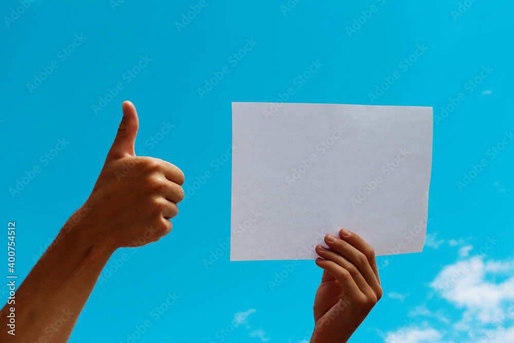 a blank sheet of paper in the hands of a young guy against a blue sky with clouds